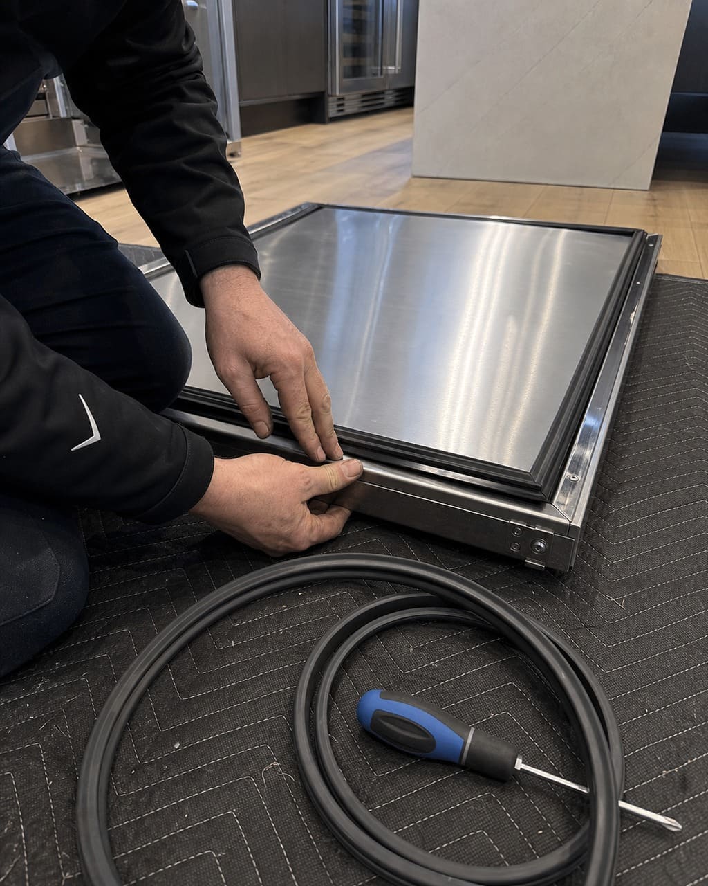 Technician replacing the door gasket and checking the drain channel on a pulled-out built-in Sub-Zero in a Cupertino kitchen